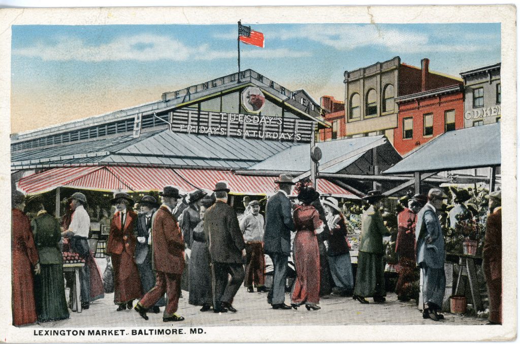 Colorized postcard of people standing around market stalls in front of the Lexington Market shed building.