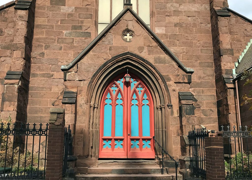 The entrance to a brownstone Gothic church building with a light blue and red door.