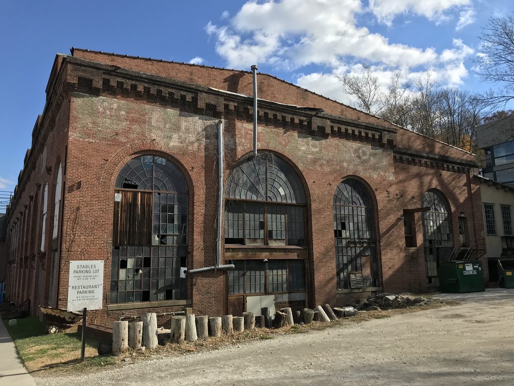 A large brick industrial building with three tall arched opening filled with a grid of small window panes.