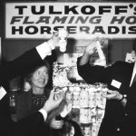 Black-and-white photo of three people holding bottles of Tulkoff's flaming hot horseradish.