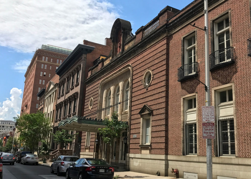 A streetscape showing a brick former theater building next to a large brownstone house.